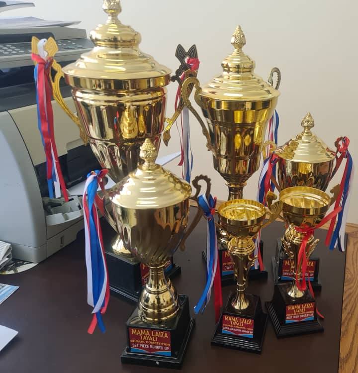 Gold trophies with ribbons, with plates reading Set Piece Runner Up, Choir Conductor Runner Up and Best Choir Conductor